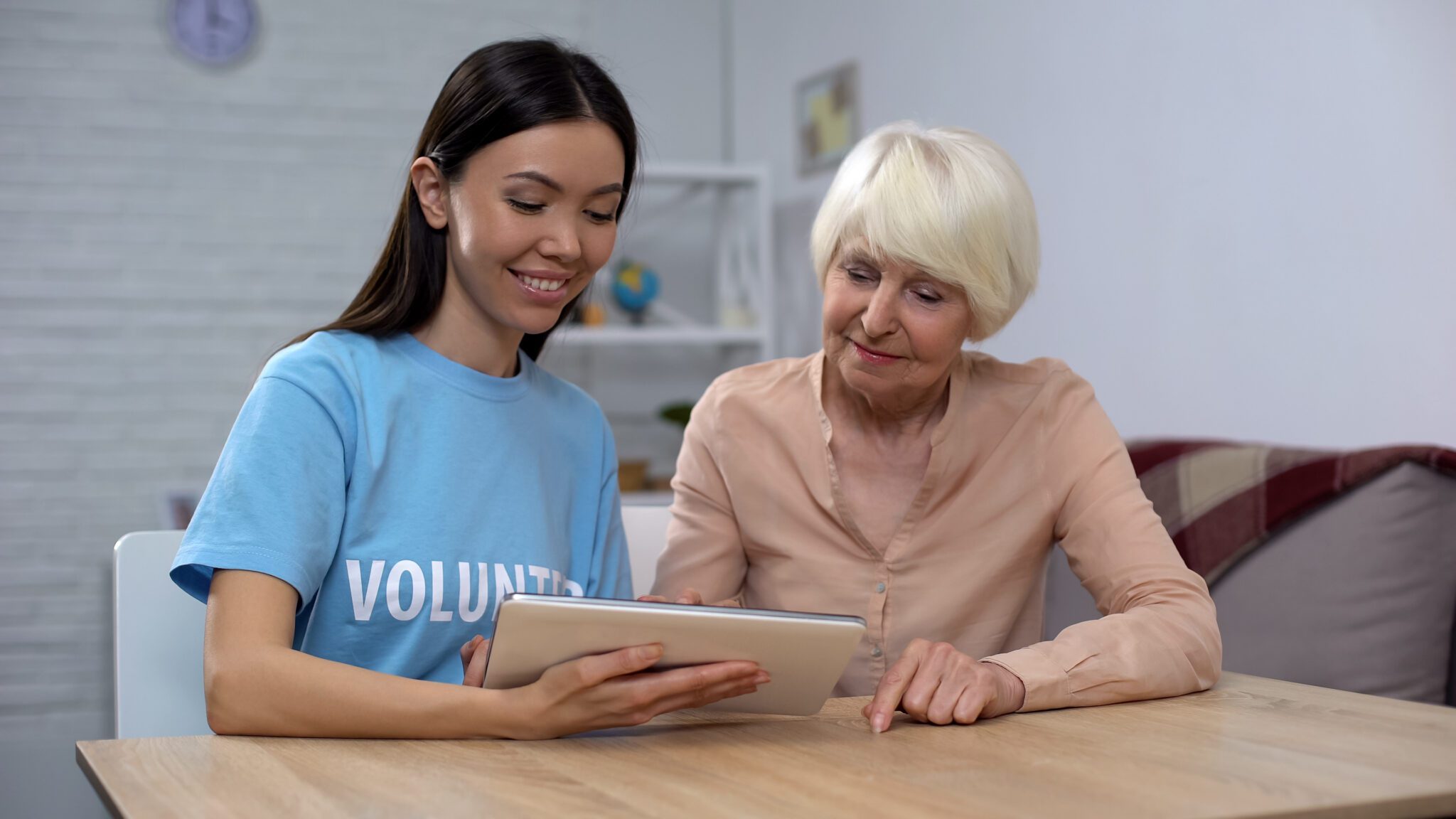 Volunteer helping elderly woman with tablet.