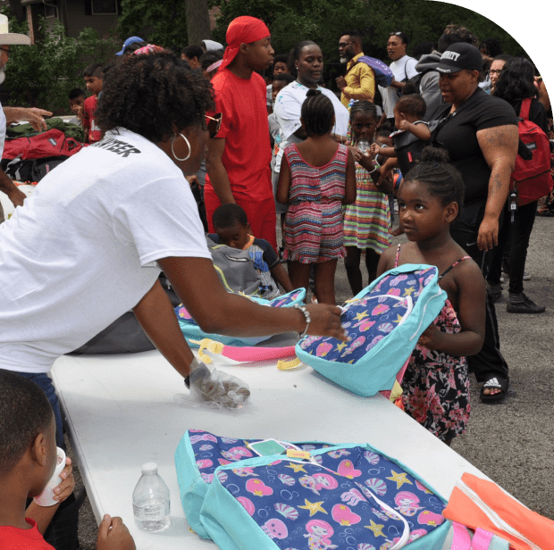 Children receiving backpacks at outdoor event.